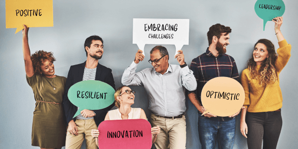 A group of 6 people in a row holding different signs with word on that depict a growth mindset.